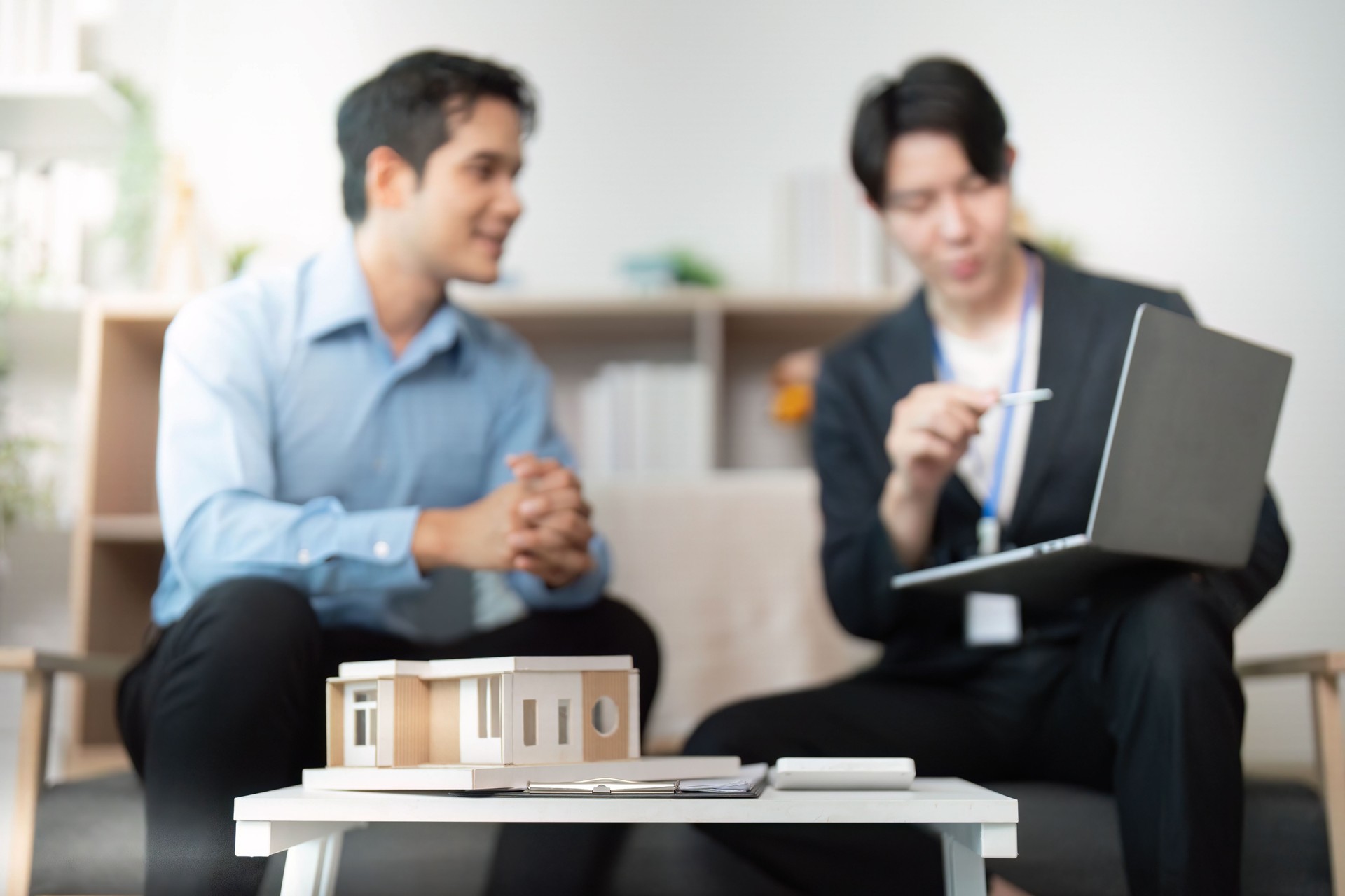 Real Estate Consultation. Two professionals discussing property plans with a model house.